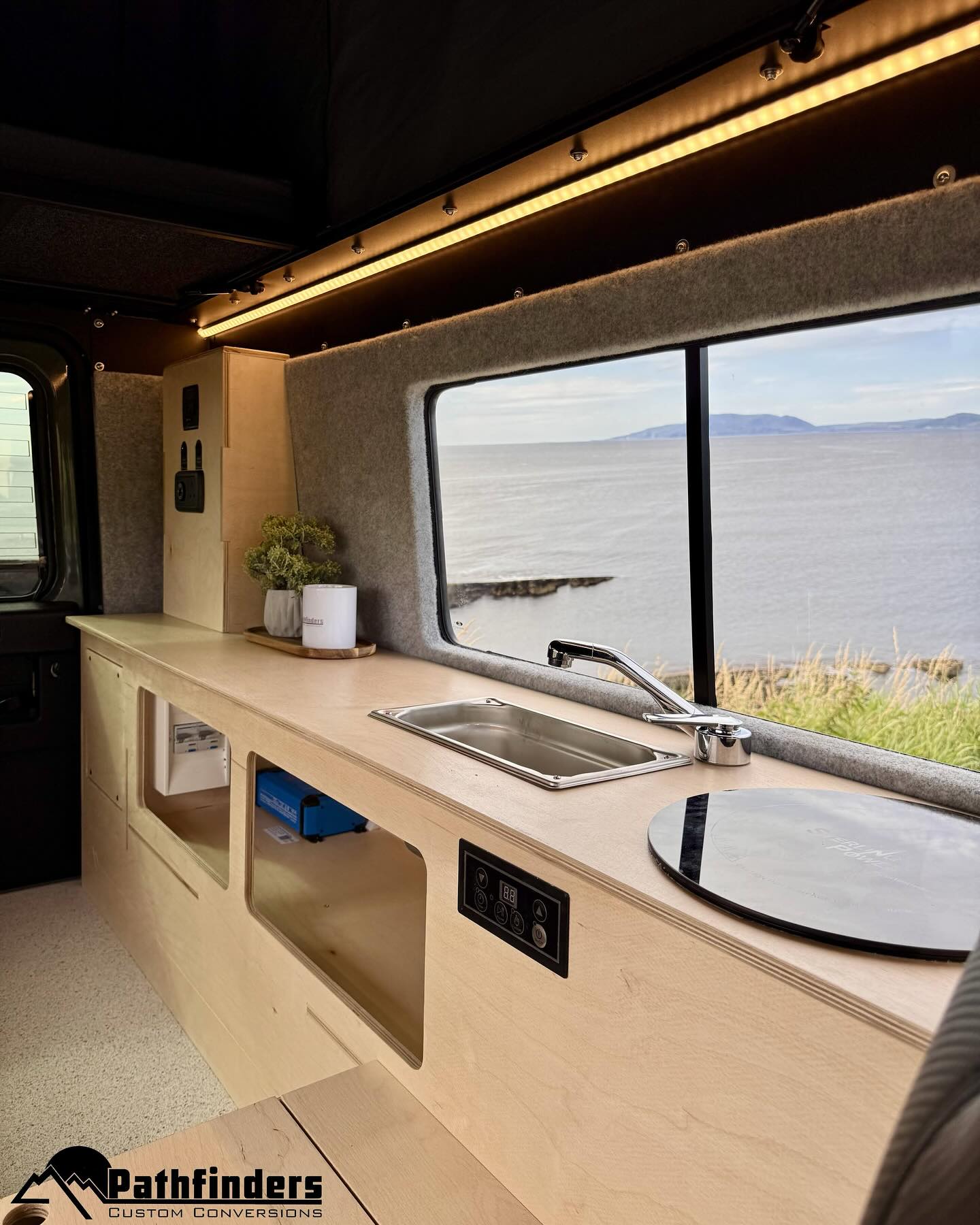 custom built kitchen unit with sink and hob and a big window with the sea in the back